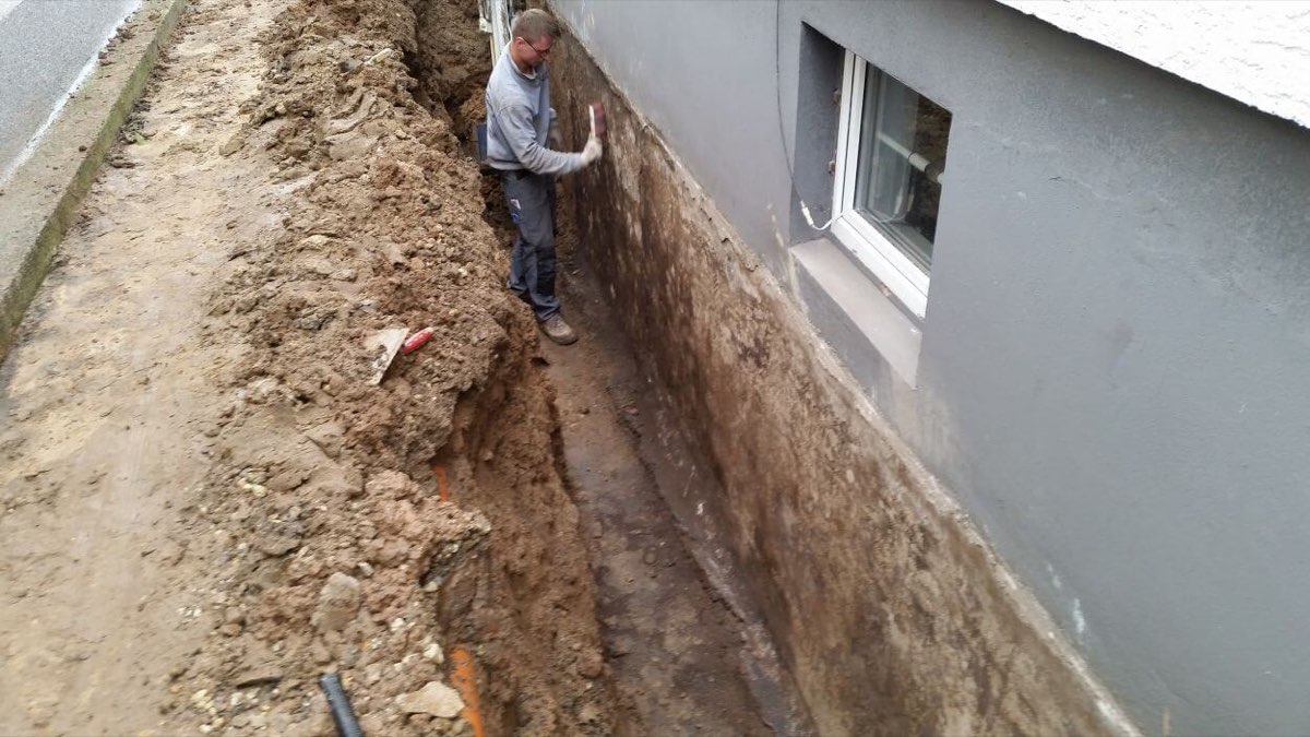 Freigelegte Kelleraußenwand in einem ausgehobenen Graben